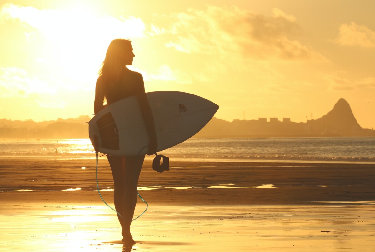 Surfer Girl am Stand mit Sonnenuntergang im Hintergrund