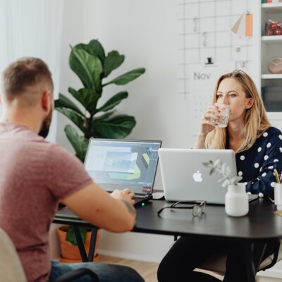 New Work im Home Office sitzt sich im Wohnzimmer an einem Tisch ein Pärchen gegenüber