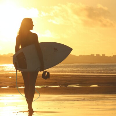 Surfer Girl am Stand mit Sonnenuntergang im Hintergrund